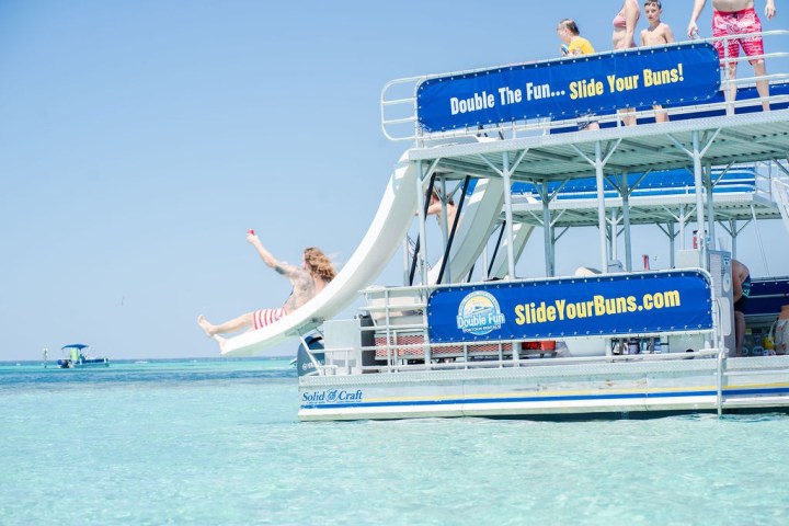 Person sliding off a boat slide into clear blue water.