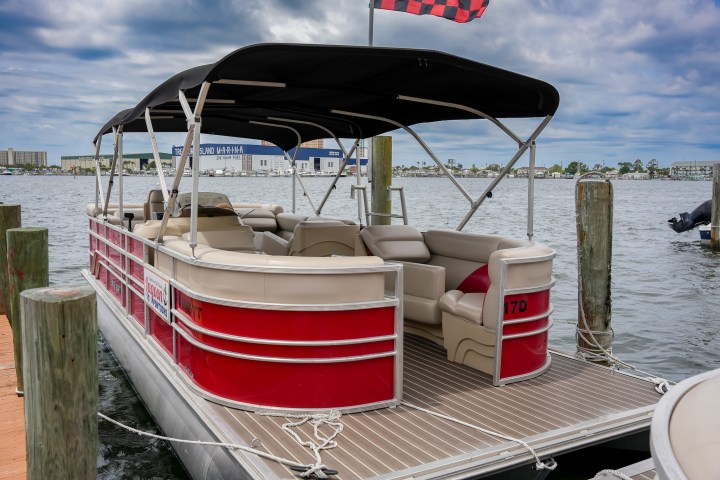 Red pontoon boat docked at marina with cloudy sky.