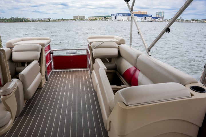 Interior of a pontoon boat with beige seating overlooking a body of water.