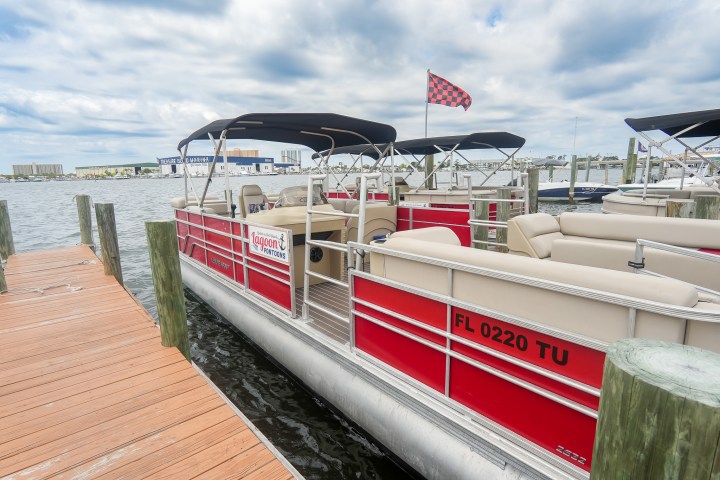 Red pontoon boat docked on a wooden pier under cloudy sky.