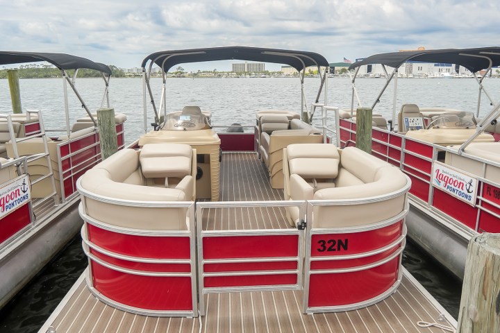 Docked red and beige pontoon boat with canopy under cloudy sky.