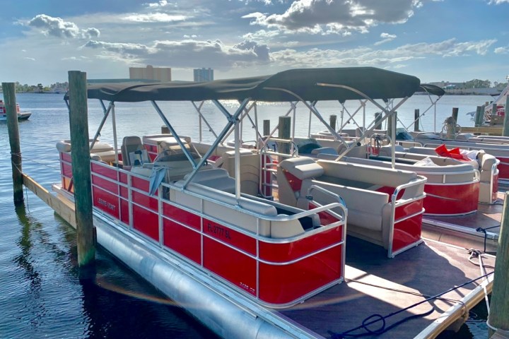 Red pontoon boats docked on a sunny day with a few clouds.