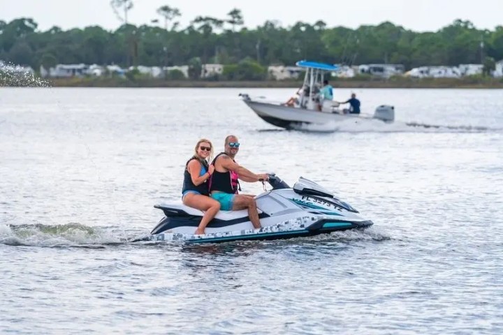 Two people on a jet ski, with a boat in the background on a lake.