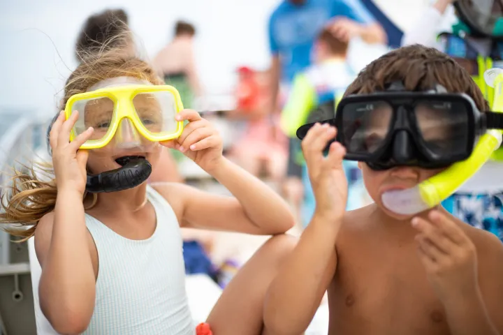 Two children wearing snorkel masks on a boat.
