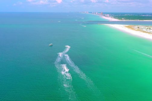 Aerial view of boats leaving trails in clear blue-green ocean near a sandy coastline.