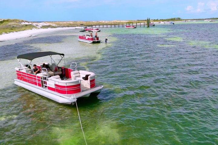 Red pontoon boat anchored in shallow water near a sandy beach.