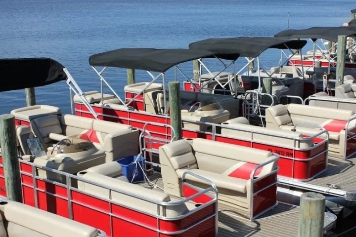 Docked red pontoon boats with black canopies on a calm lake.