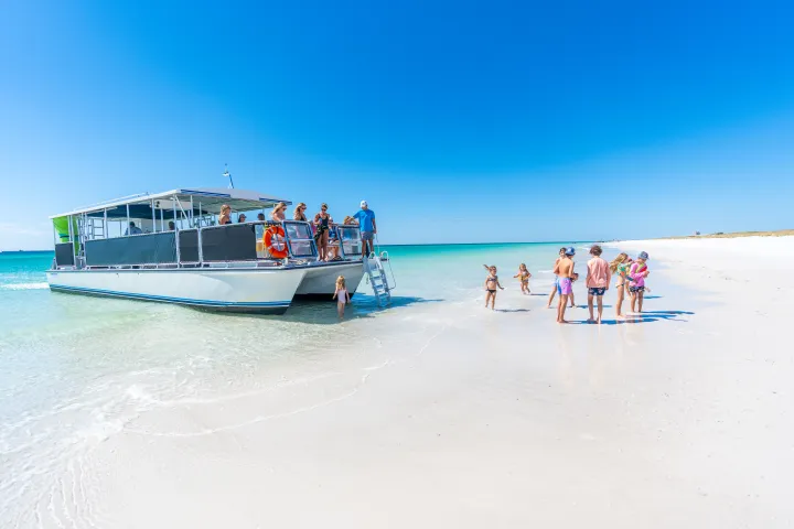 A group of people on a boat docked at a white sandy beach under a clear blue sky.