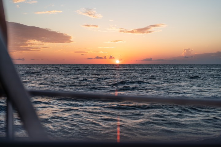 Sunset over ocean with partially cloudy sky and boat railing in foreground.