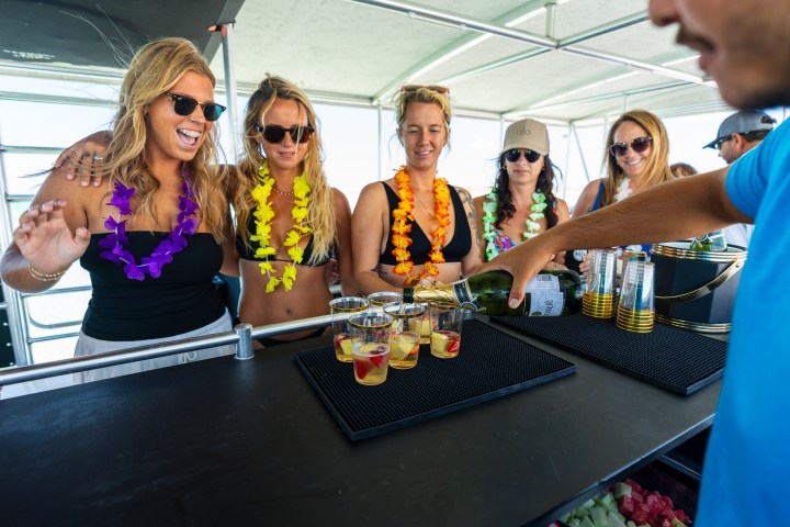 Group of women in leis at a bar with drinks, bartender pouring champagne.