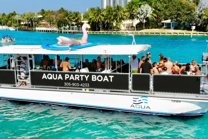 Party boat on turquoise water with people and a pink flamingo float.