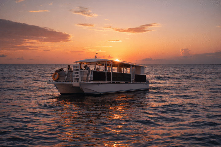 A boat on the ocean at sunset, with a colorful sky and calm waters.