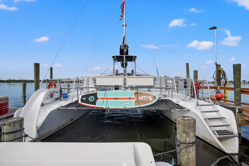 A catamaran docked with a paddleboard on its stern, under a blue sky with scattered clouds.