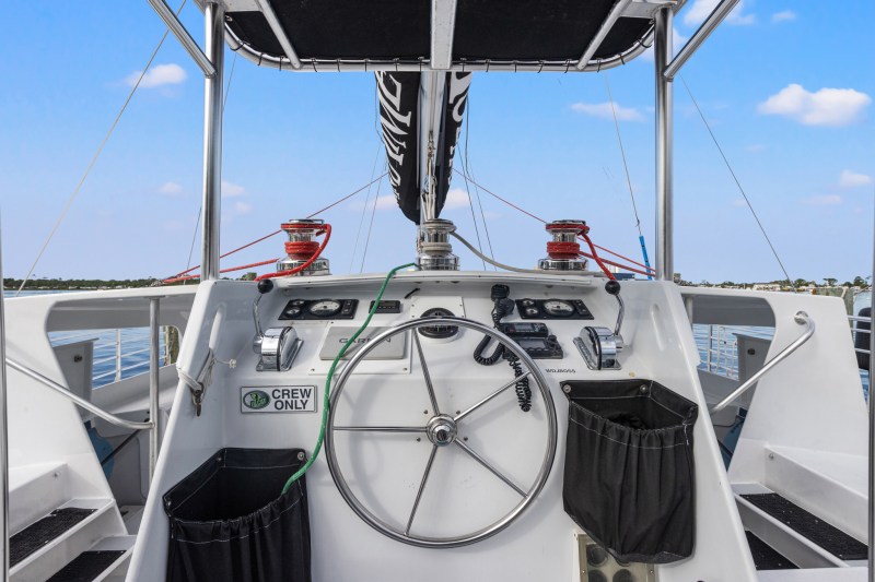 Boat steering wheel and control panel with 'Crew Only' sign, view of water and land.