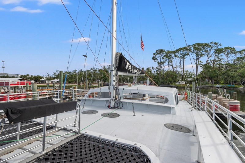 View from sailboat deck with mast, railings, and trees in background.