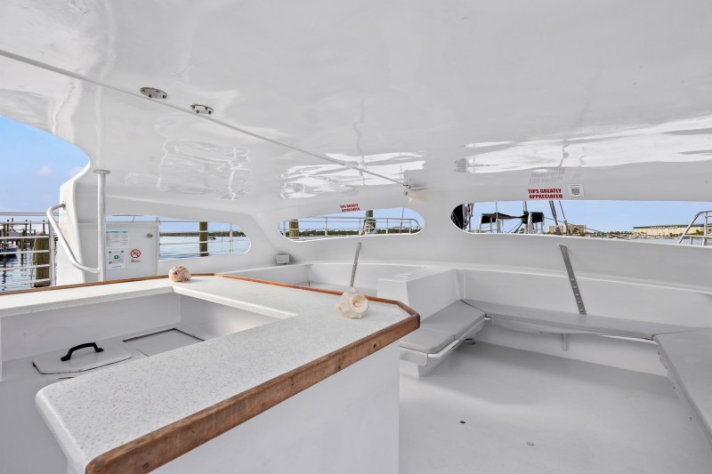 Interior of a white boat with seating, tables, and shell decorations under a covered area.
