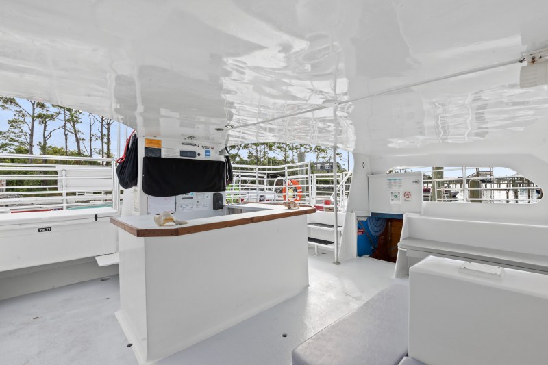 White boat interior with benches, a counter, and outside view of trees and marina.