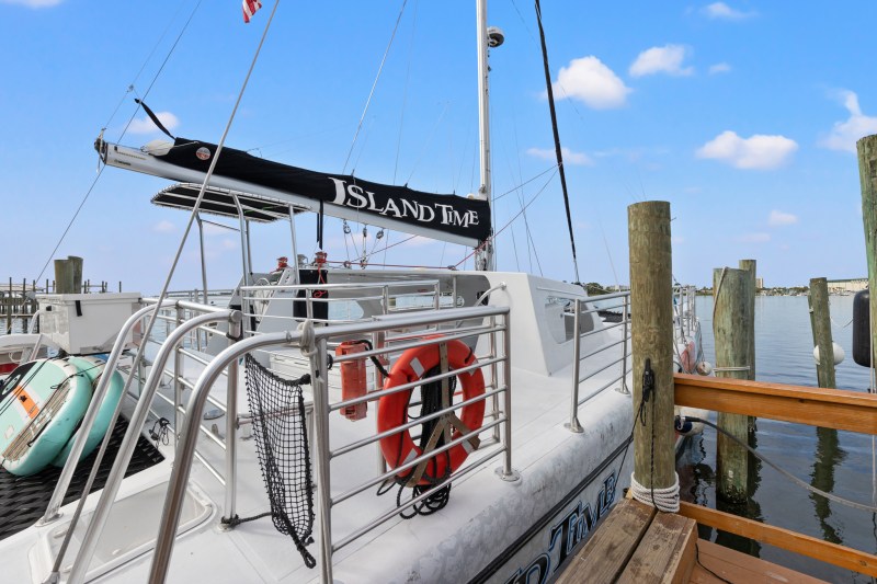 Docked sailboat named Island Time with life buoys and clear sky backdrop.