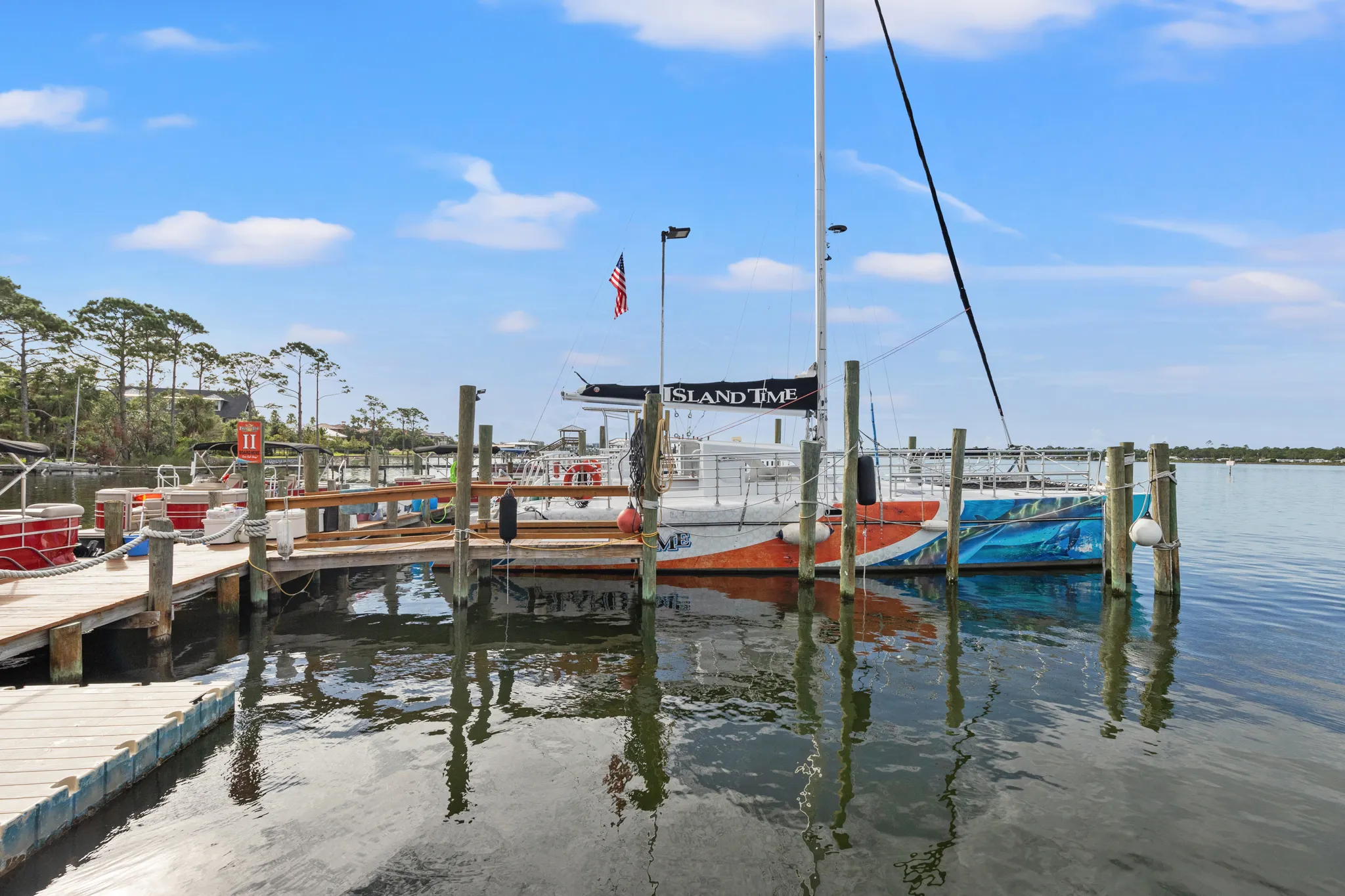 Docked sailboat with 'Island Time' banner, surrounded by calm water and trees under a clear sky.