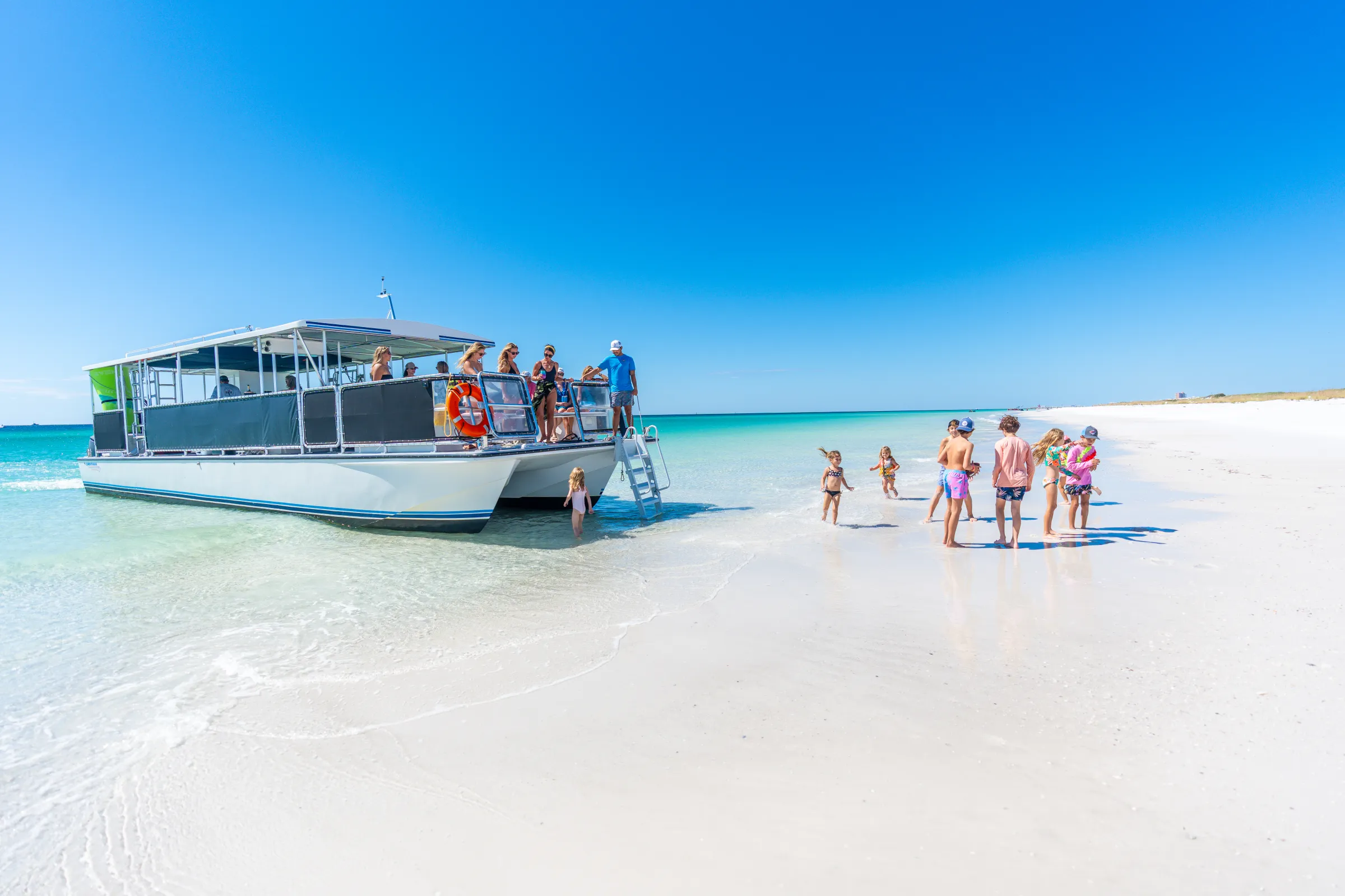 People on a boat and children playing on a sunny beach with clear water and blue sky.