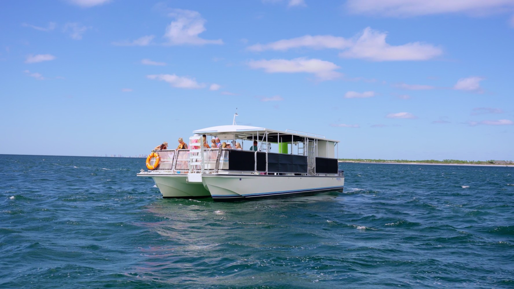 A boat with people sails on a vast, blue ocean under a partly cloudy sky.