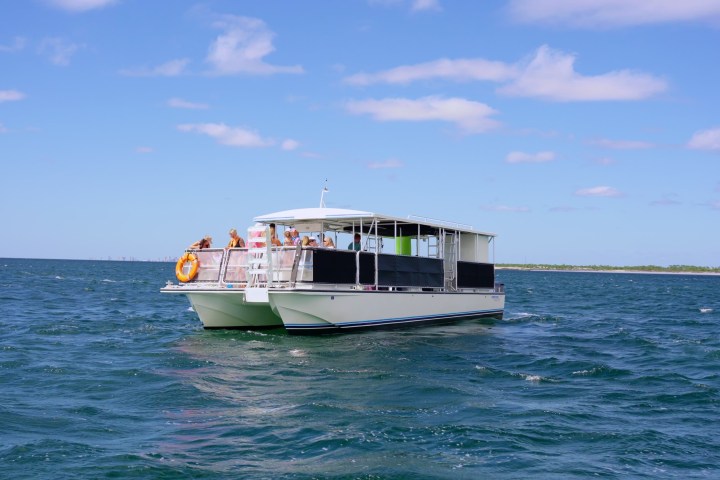 A boat with people sails on a vast, blue ocean under a partly cloudy sky.