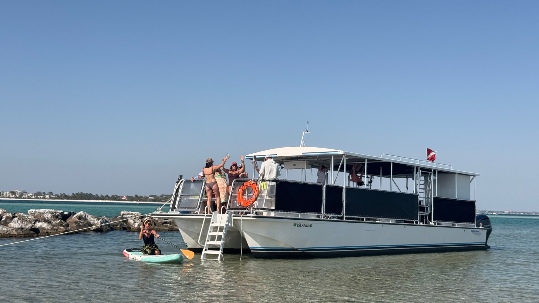 Tour boat anchored near shore with people on deck and swimmers nearby.