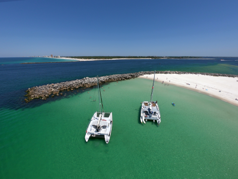 Two catamarans on turquoise water near a sandy beach with clear blue sky.