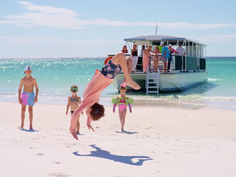 Person doing a flip on a sunny beach near a boat.