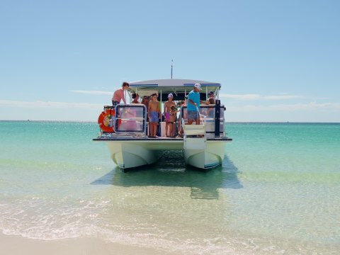 Group on a catamaran docked at a sandy beach with clear turquoise water.
