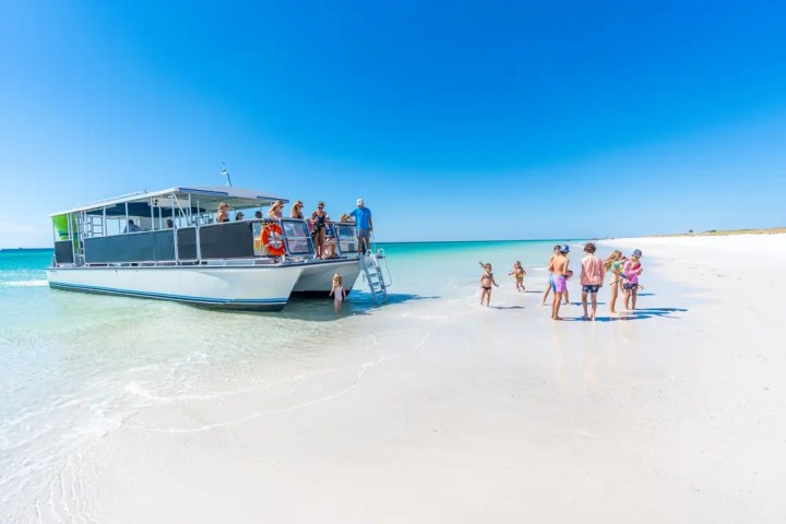People on a boat and beach under clear blue sky.