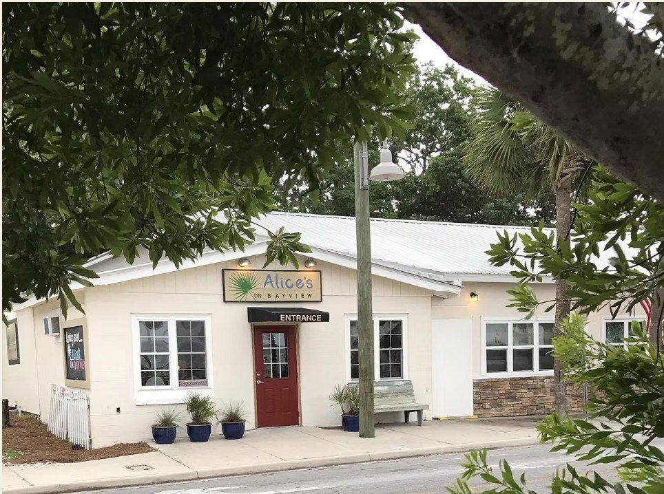 Small restaurant with red door, labeled 'Alice's Diner,' surrounded by trees.