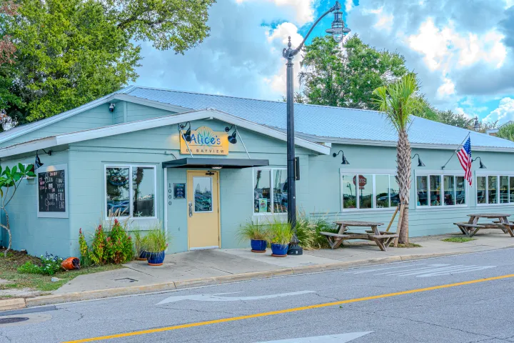 Light blue diner with outdoor seating, American flag, and greenery on a cloudy day.