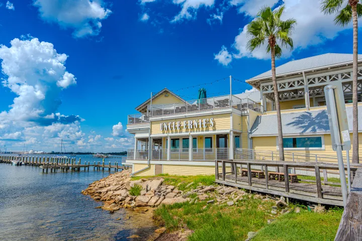 Waterside restaurant with palm trees and bright blue sky.