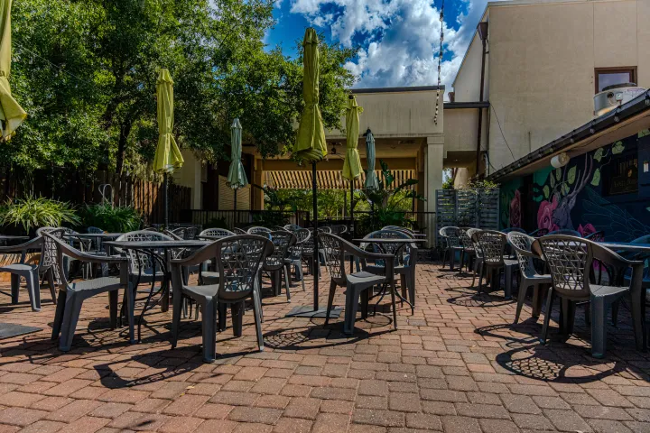 Outdoor patio with empty tables and chairs under green umbrellas.