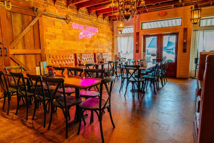 Rustic restaurant with wooden tables, chairs, and neon wall sign.